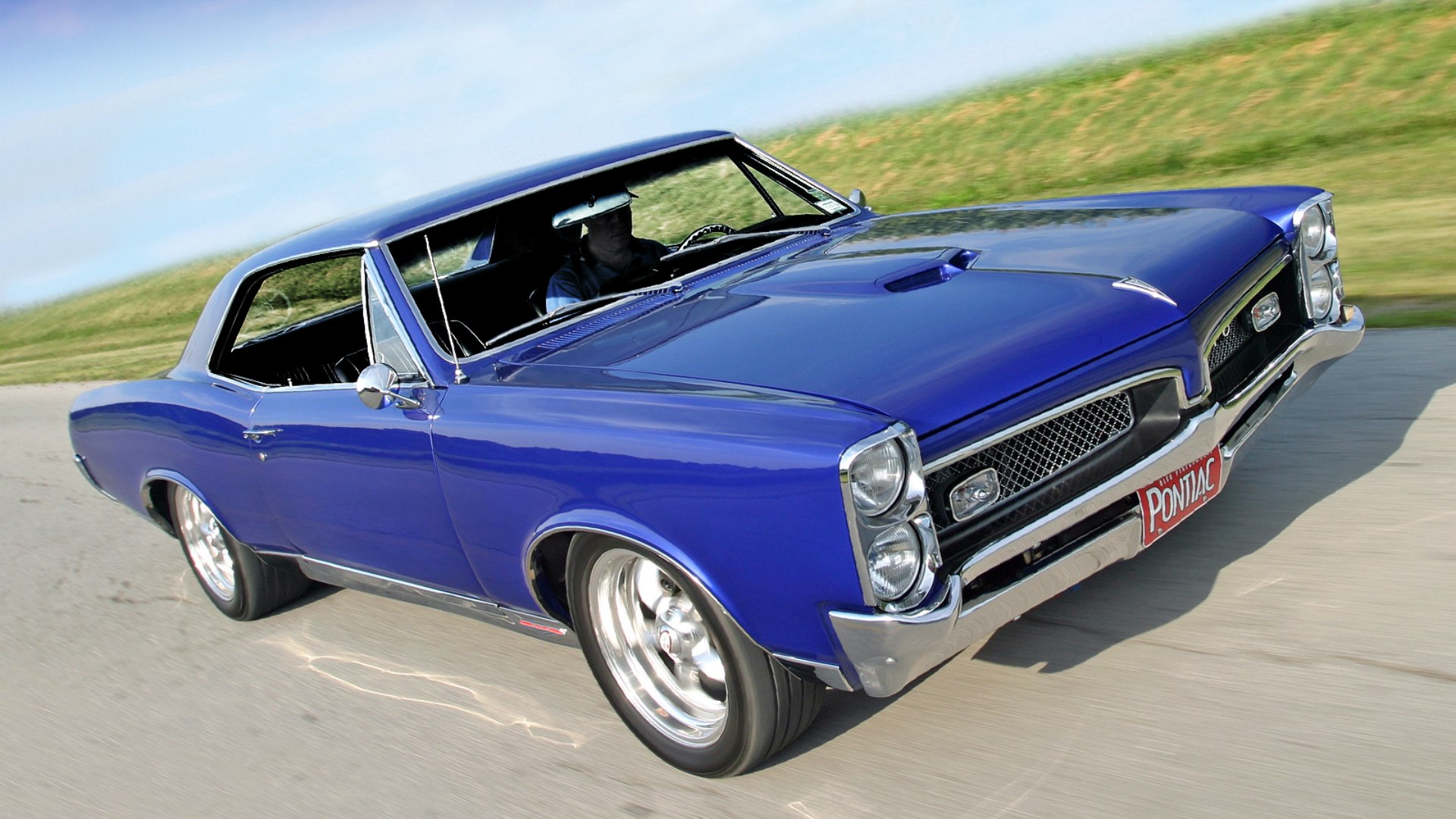 Синий Pontiac GTO разгоняется на прямой дороге с отличной видимостью